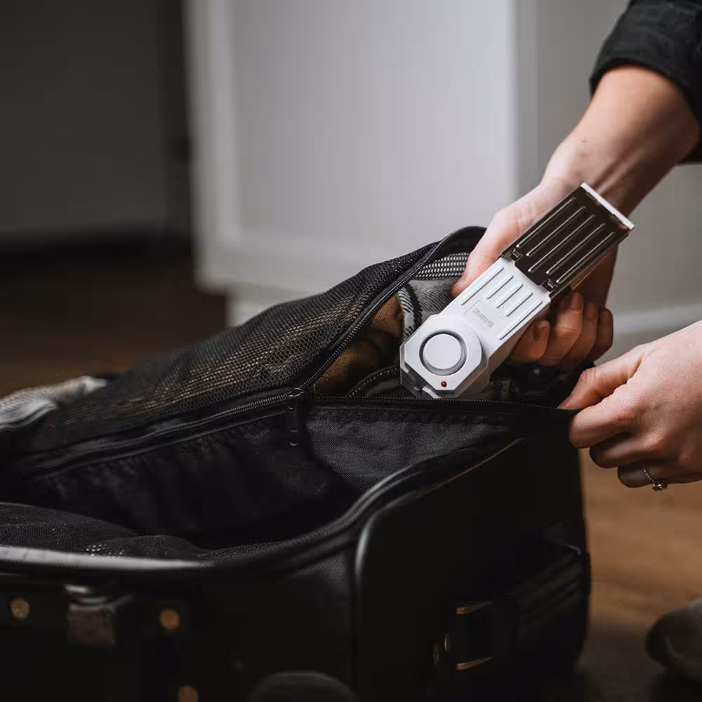 Person holding the SABRE home security door alarm over an open suitcase