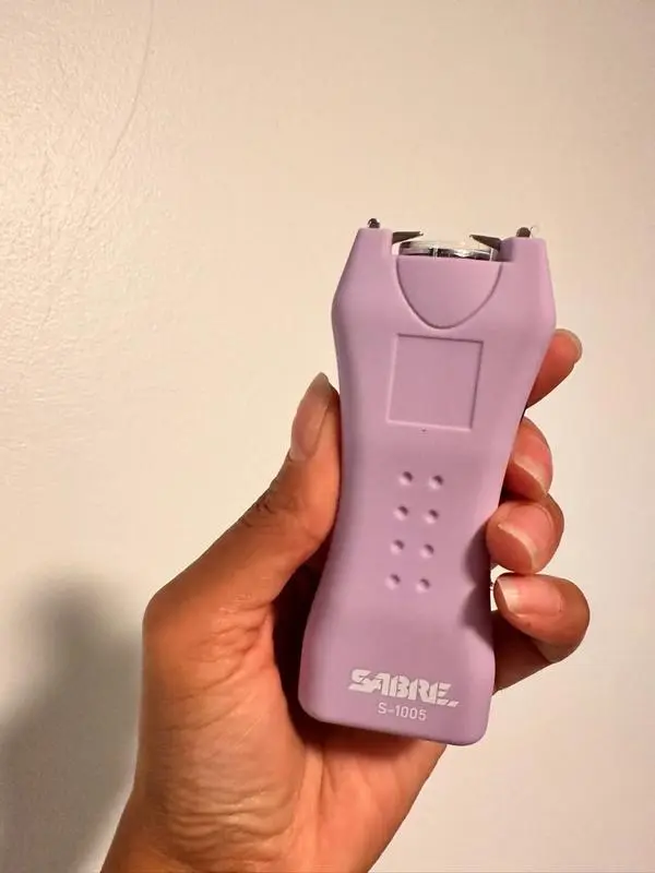 A person holding a SABRE stun gun and flashlight